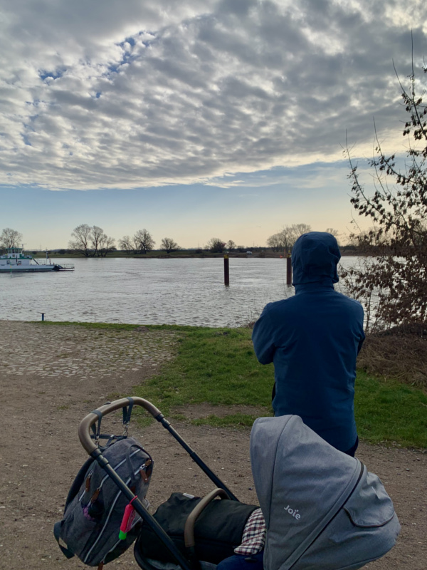 Ein Mann und ein Kinderwagen blicken auf einen Fluss